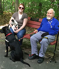 Man, woman and two dogs sit on bench.