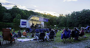 Outdoor stage with audience sitting in lawn chairs.