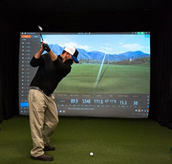 Man hitting golf ball in front of screen.