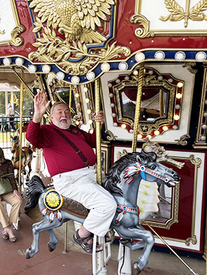 Wayne Valis waving while riding on carousel at Chessie's Big Backyard in Fairfax County VA.