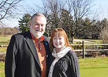 Wayne and Angela Valis stand in fenced field.